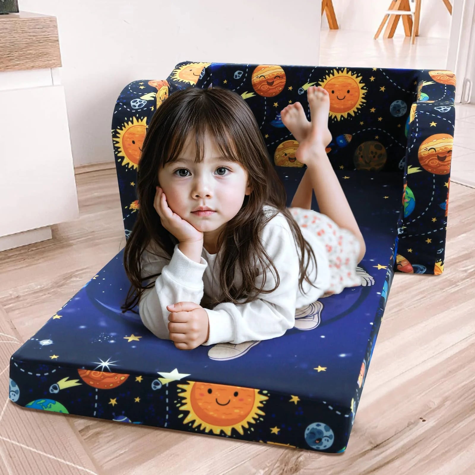 A little girl lying on an unfolded Glowsofa's Children's fold out sofa with Astronaut patterns