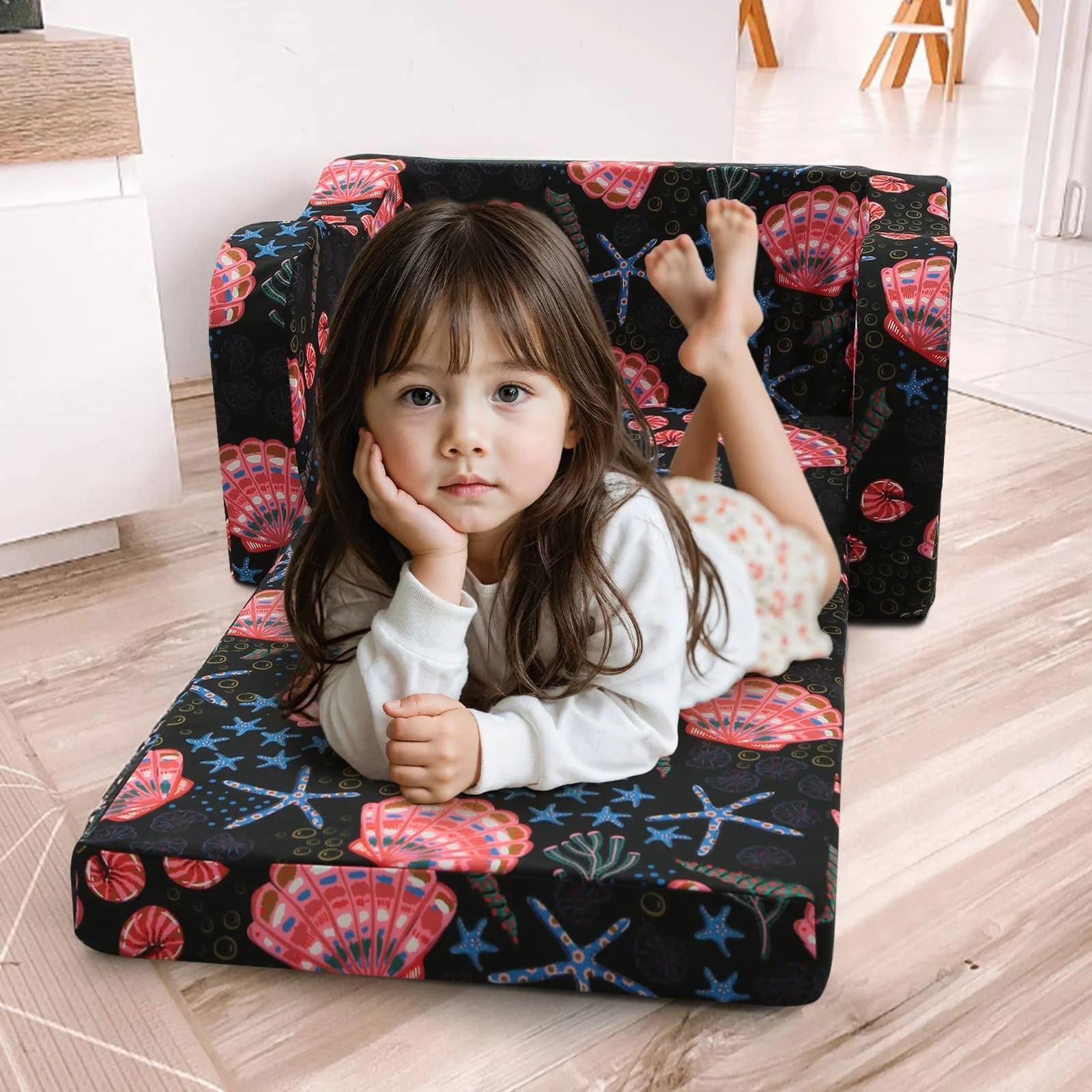 A little girl lying on an unfolded Glowsofa's Children's fold out sofa with Seashell patterns