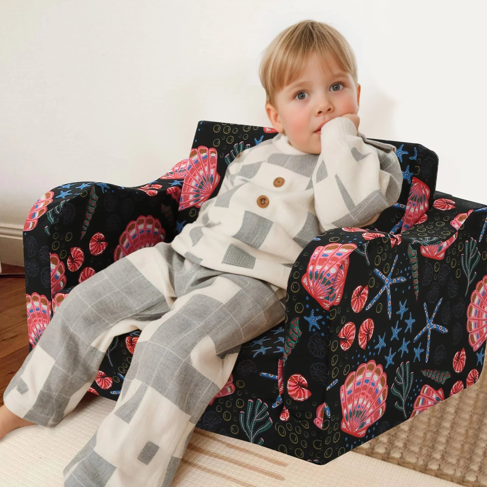 A boy sitting in Glowsofa's children's couch chair with Seashell patterns 