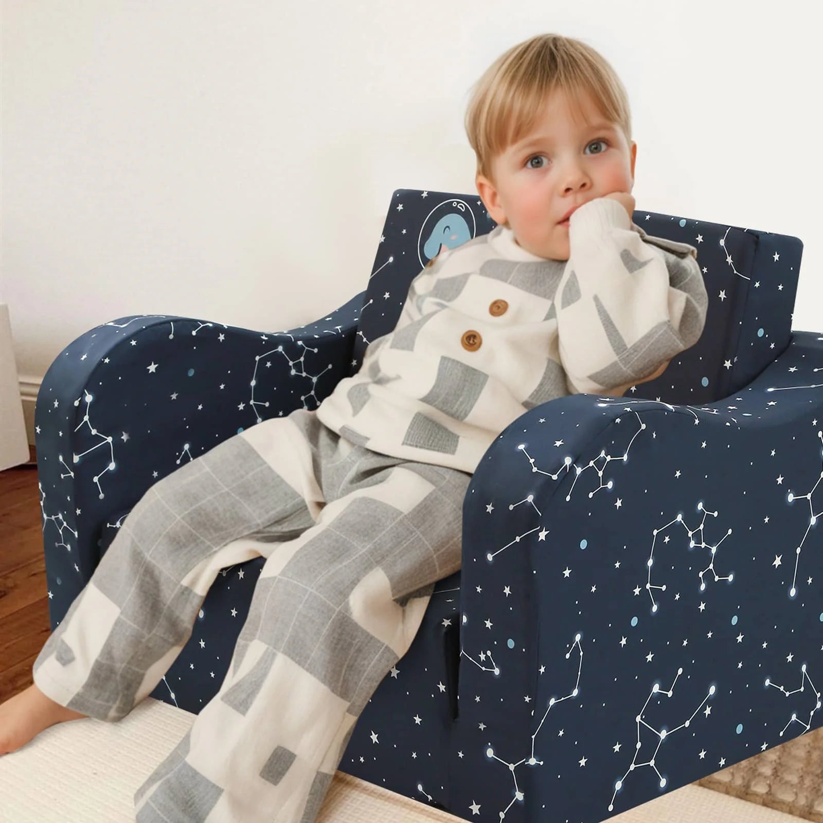 A boy sitting in Glowsofa's children's couch chair with Space Dinosaur patterns 